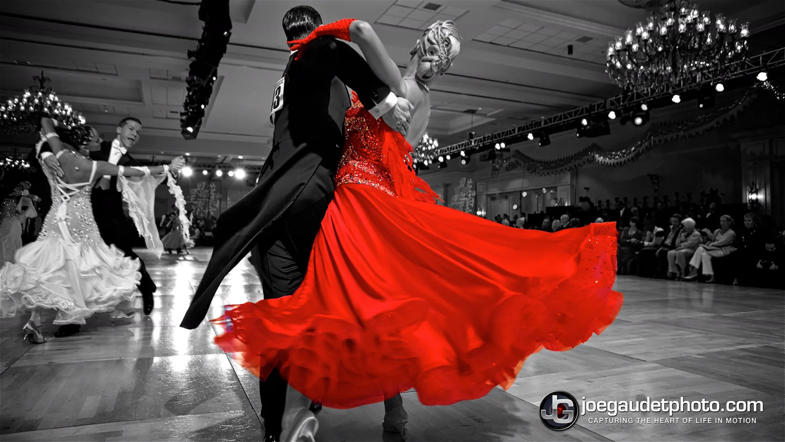 A ballroom couple mid-turn, her red gown flaring out while the rest of the room falls away in black and white